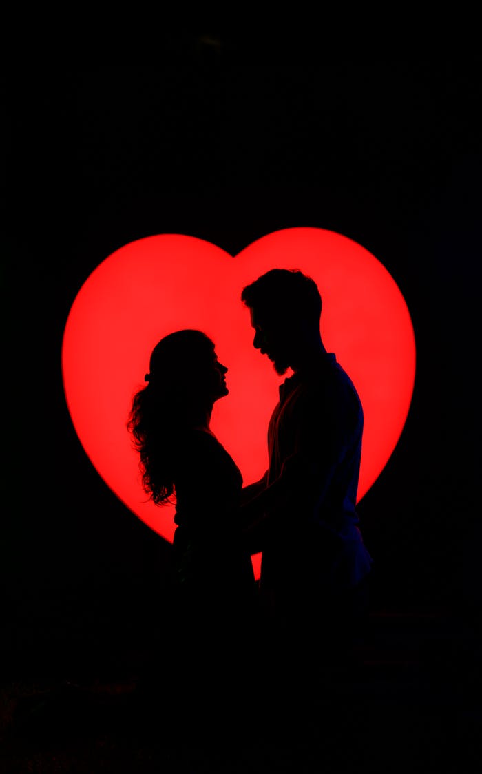 Silhouette of a loving couple embracing against a vibrant heart backdrop.